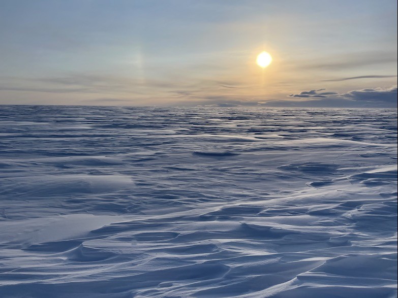 The sun hangs low in the sky highlighting the rough surface Sun on ice