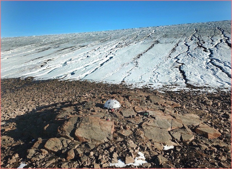 Team tent in the foreground is overshadowed by the ice sheet behind. Tent in front of ice sheet
