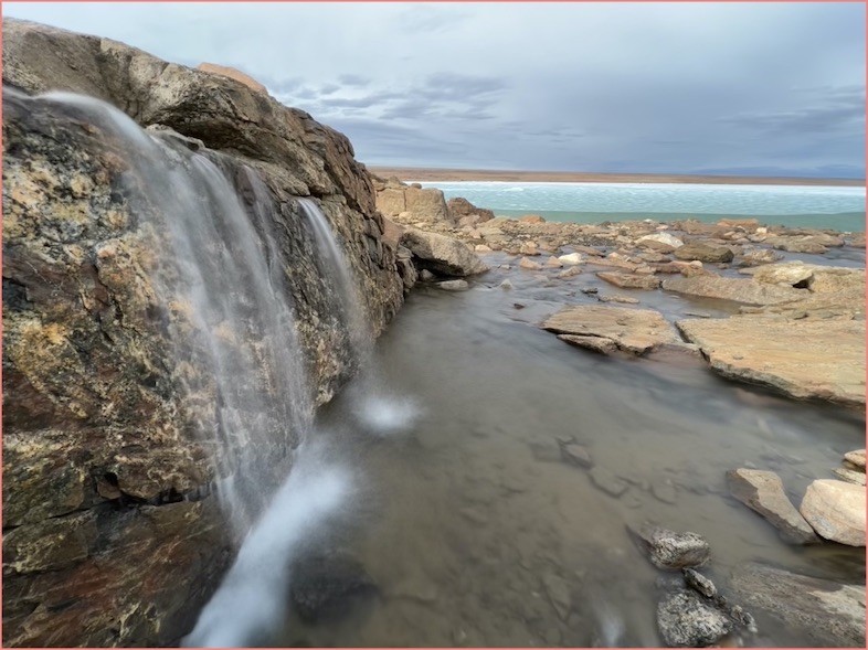 Waterfall of meltwater streaming off the rocky edge of NW Greenland waterfall